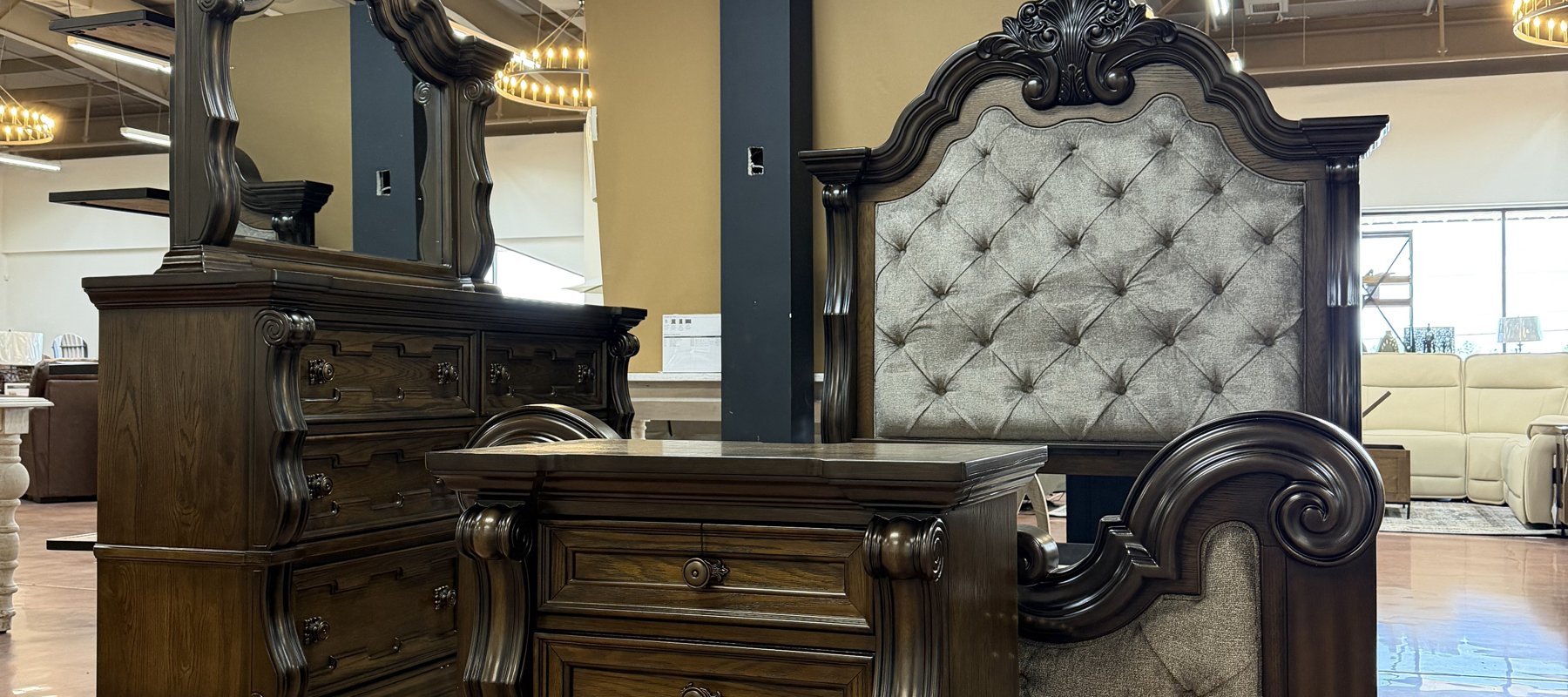 Traditional dark-wood bedroom set with a button-tufted upholstered headboard, mirrored dresser, and nightstand on the gallery floor at Lakehouse Furniture Gallery in Osage Beach, Missouri.