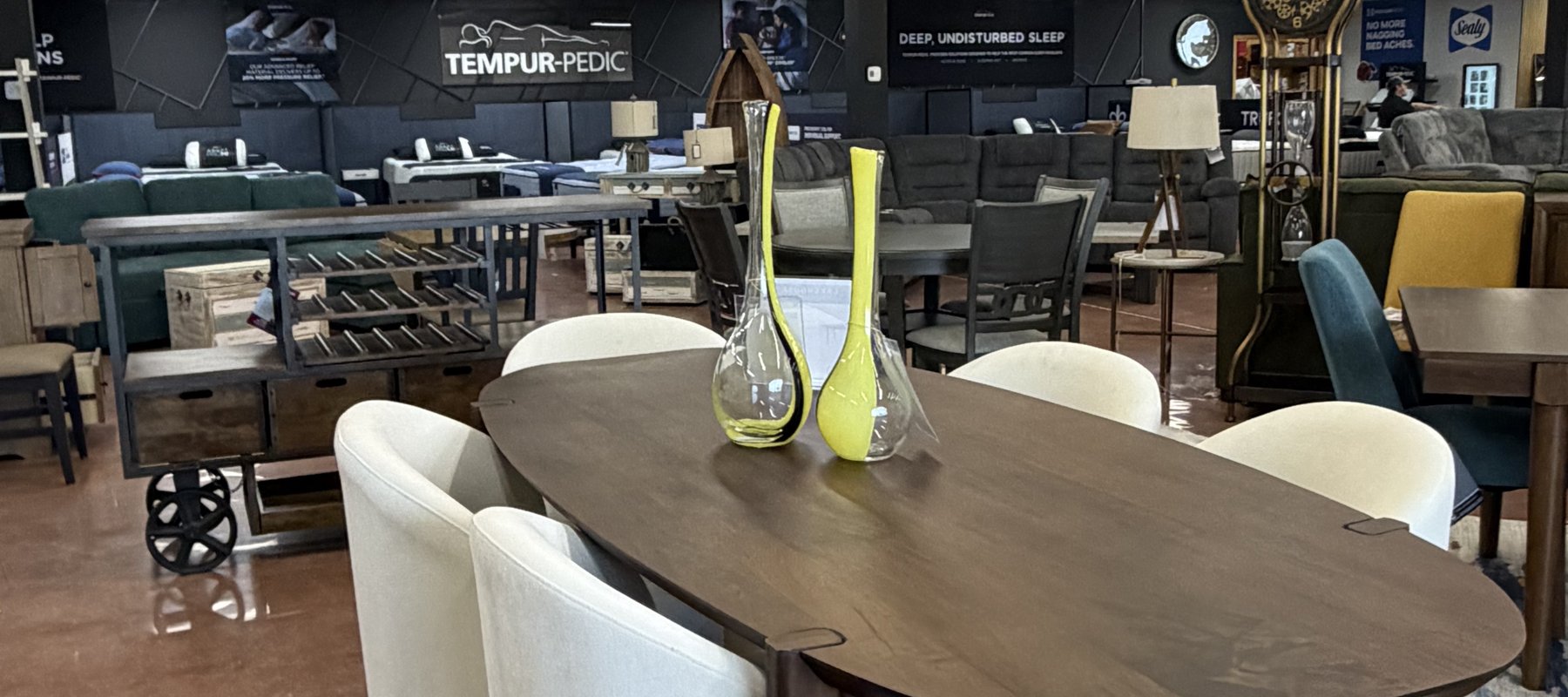 Upscale oval wood dining table with cream curved upholstered chairs and glass accents at Lakehouse Furniture Gallery in Osage Beach, Missouri.