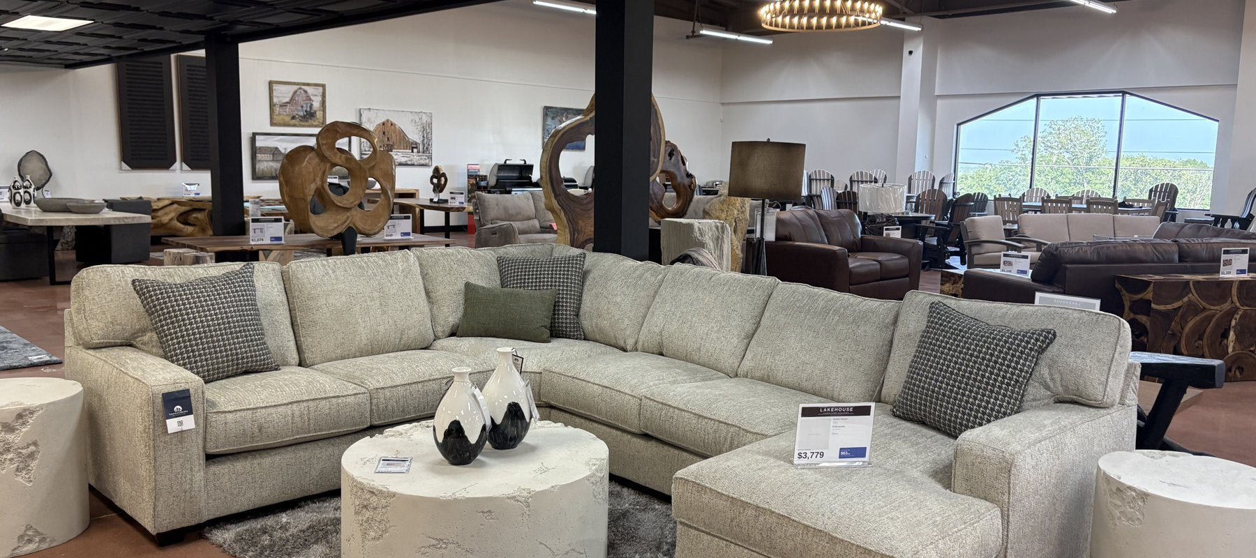 Cream fabric sectional with textured accent pillows and a round upholstered coffee table on the showroom floor at Lakehouse Furniture Gallery in Osage Beach, Missouri.