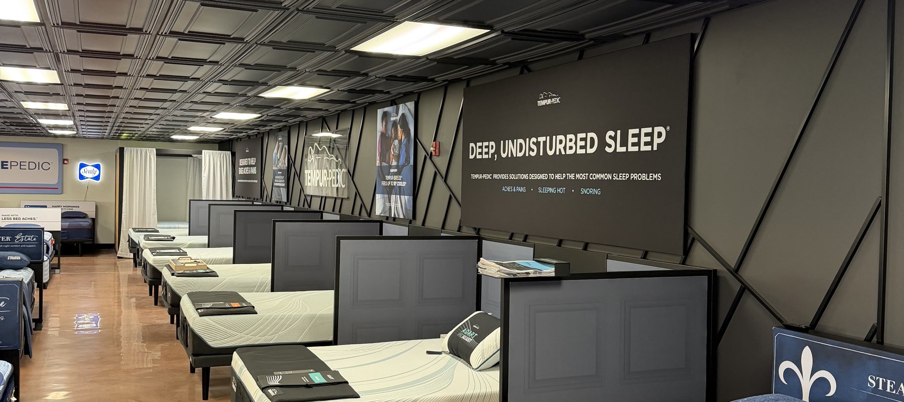 The mattress gallery at Lakehouse Furniture Gallery in Osage Beach, Missouri, with Tempur-Pedic, Sealy Posturepedic, and Stearns and Foster displays beneath a Deep Undisturbed Sleep banner.
